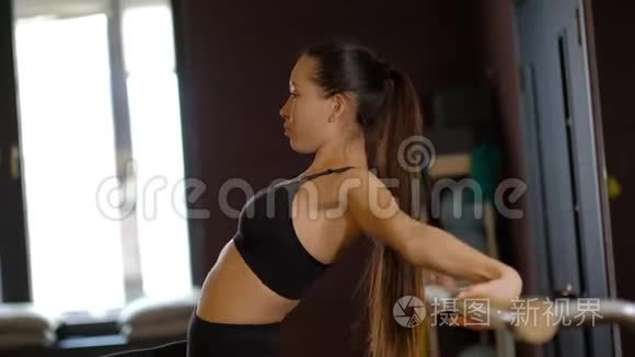 年轻的女舞蹈演员，扎着长长的马尾辫，穿着紧身衣，表现出身体的灵活性，握着芭蕾舞的扶手，慢动作