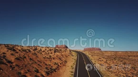 无人驾驶飞机在美国古迹谷的空旷沙漠道路和悬崖山的右侧飞行，天空晴朗。