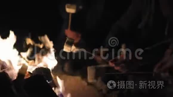 近距离观看手拿棍子与棉花糖，并在晚上煎。 一群人坐在火边