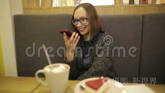 女人坐在沙发上用免提电话说话很开心。 戴眼镜的智能手机女孩喝热巧克力