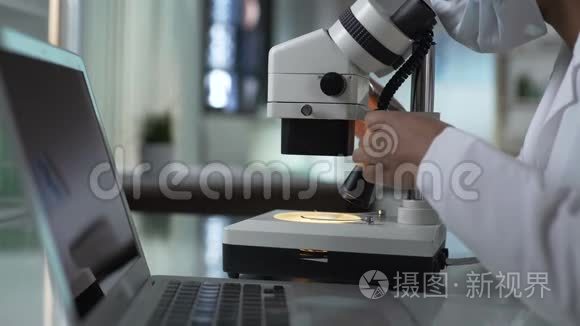 实验室工作人员在显微镜下研究样品，在电脑上输入结果