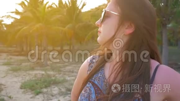 戴着蓝色帽子和眼镜的年轻女孩看着远处，在热带棕榈树的背景下微笑。慢动作。