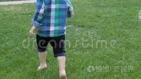 在公园里，一个可爱的蹒跚学步的男孩的脚在新鲜的绿草上奔跑