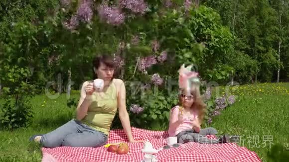 年轻的母亲和小女儿在春天的野餐旁边，一朵盛开的丁香花。