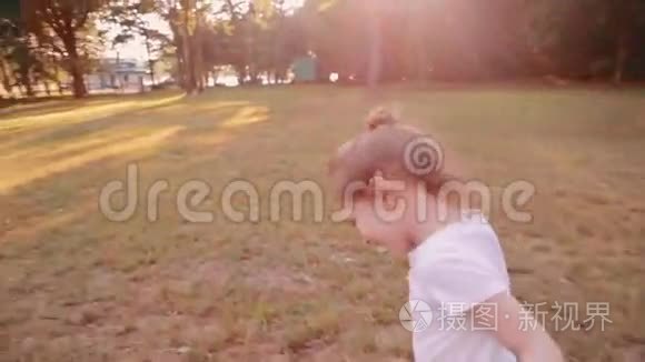 一个快乐的小女孩在阳光明媚的夏天在公园的一条路上跑步。 后景，慢影