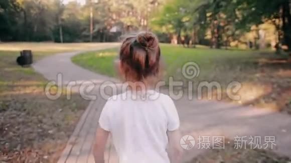 小女孩在公园的路上散步。 一束美丽的头发在阳光下闪闪发光。 慢影，后景