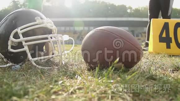 美国足球运动员站在球场上，球和头盔躺在草地上