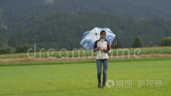 一位年轻女子撑着伞走在田野上视频