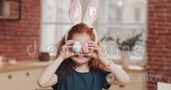 欢快的红头小女孩的肖像，带着兔子耳朵，厨房背景上有一个复活节彩蛋。 她是