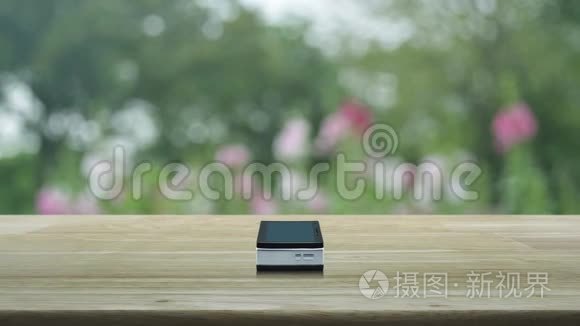 现代智能手机屏幕上的麦克风平板图标在木桌上，在公园的粉红色花朵和树木上模糊，商务交流。
