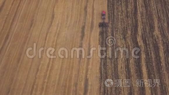 空中：在耕地上向无人机射击。一辆红色拖拉机在秋天开垦田地