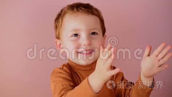 可爱的小红头发男孩微笑着，双手拍在粉红色的背景上
