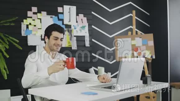 年轻的商人戴着耳机，用网络摄像头说话，看着笔记本电脑