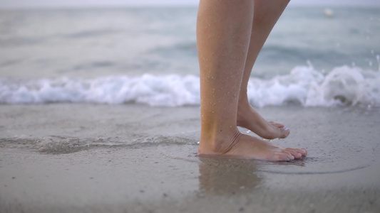 在夏日海滩上沿着海水和沙子的潮流行走的年轻女子紧紧视频