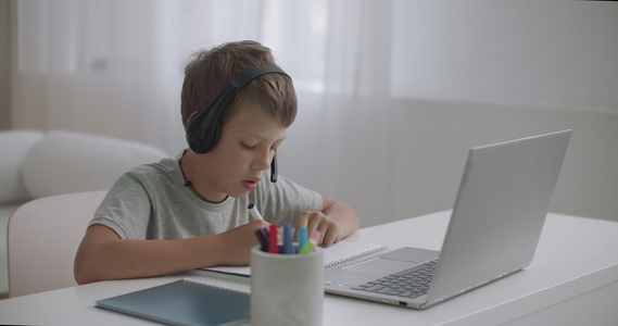 小男孩正在看笔记本电脑上为儿童播放的教育录像用耳机视频