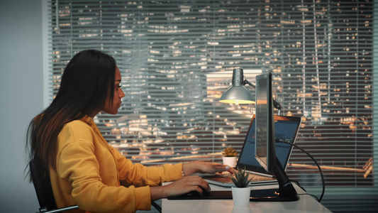 黑人女性摄像师的侧面视图用两个显示器在计算机上播放视频