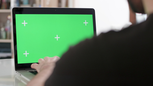 一个用绿色屏幕在笔记本电脑上工作的人的肩膀被射中视频