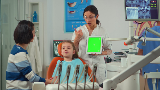 站在女病人旁边的儿科牙医站着指着绿色屏幕显示器视频