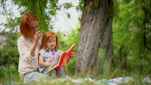 快乐的年轻母亲与女儿一起在户外阅读27秒视频