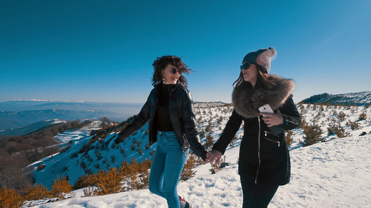 两个美丽快乐的青少年在山上的冬雪上微笑和行走的电影视频