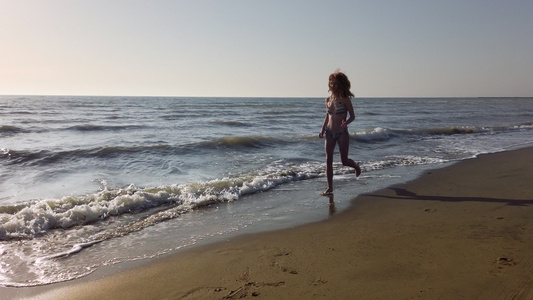 穿着比基尼的快乐美丽的双影女孩在日落时在海滩上奔跑视频
