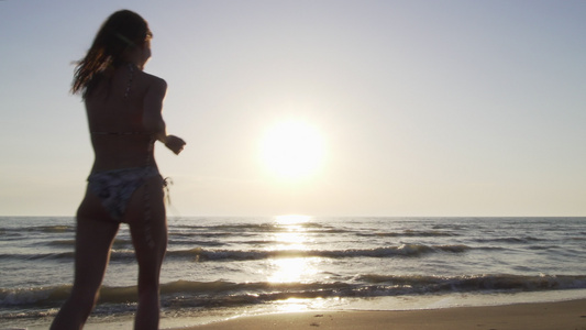 日落时在海滩上穿比基尼的月光女孩在水中奔流跳跃视频