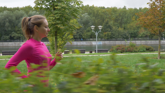 年轻的caucasian女子正在绿公园沿灌木丛跑步视频