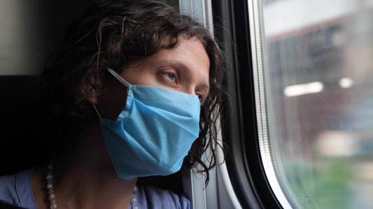 一位戴着蓝色防护面罩的疲惫中年妇女望向火车窗外戴着视频
