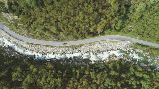 夏日汽车在挪威山沟的乡间小路上行驶河和绿山坡空中垂直视频