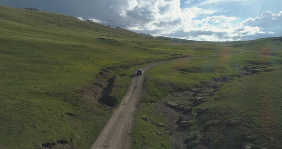 SUV车在夏日的绿色山丘沿碎石路行驶空中观察无人驾驶视频