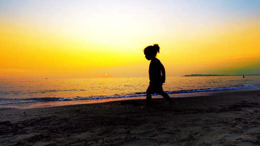 年轻男孩在空沙滩上行走的脚影其背景是夏季日落电影史视频