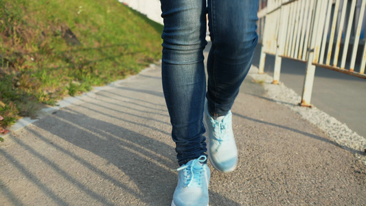 在阳光明媚的城市穿着蓝色牛仔裤和运动鞋的慢动作女性视频