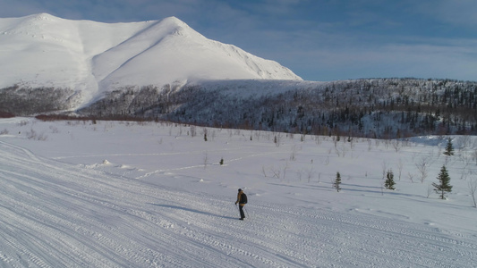 男子在晴朗的冬日在山上徒步旅行并使用登山杖鸟瞰图无人机视频