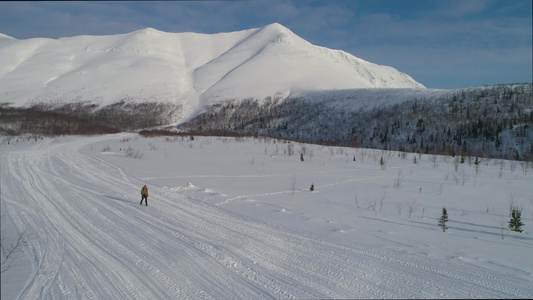 男子在晴朗的冬日在山上徒步旅行并使用登山杖鸟瞰图无人机视频