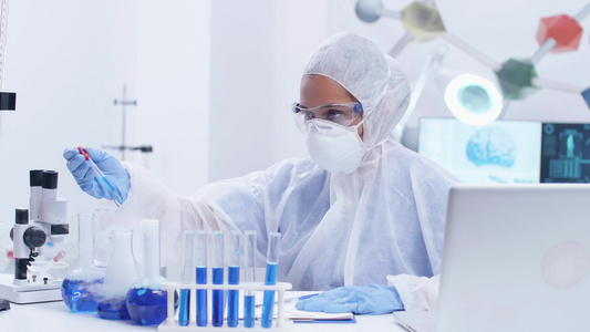 专注于工作服防护设备的女科学家用吸蓝色液体进行科学视频