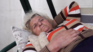 坐在门廊摇摆床上的老年妇女躺着看着悲伤的距离17秒视频