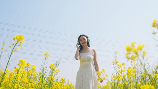 长裙女人在油菜花田里带耳机听音乐视频