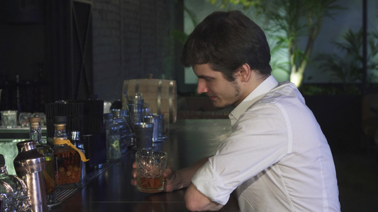 年轻帅哥独自在酒吧里喝威士忌对着镜头开心地微笑视频