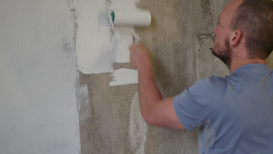 油漆期间墙上的油漆滚筒用白色翻新建筑墙壁英俊的年轻视频