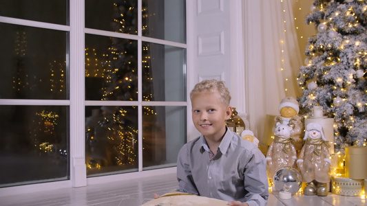 金发男孩把圣诞礼物盒扔在圣诞节树底的圣诞树上视频