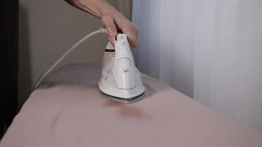 一个男人用白电铁在熨衣板上烫床单视频