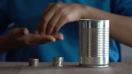 穿着蓝衬衫的女人把一枚硬币扔进老罐子里在棕色木制桌子视频