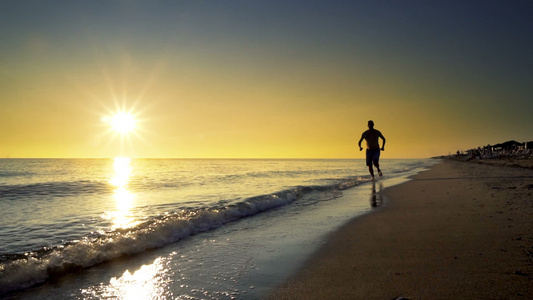 一只年轻男慢跑者在日落时在海边奔跑慢动作视频