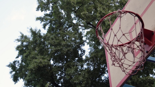 投掷的橙色篮球在树荫下的户外球场上干净利落地击中篮筐视频