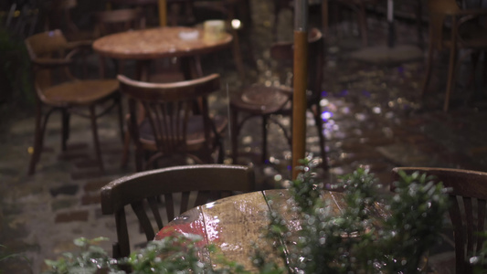 夜间大雨中的街头咖啡馆湿木家具桌椅雨滴落在桌上闪闪发光视频