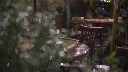 夜间大雨中的街头咖啡馆湿木家具桌椅背景的无法辨认的视频