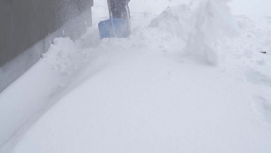 用蓝色的铲子缓慢移动地把房子周围的雪拿起视频