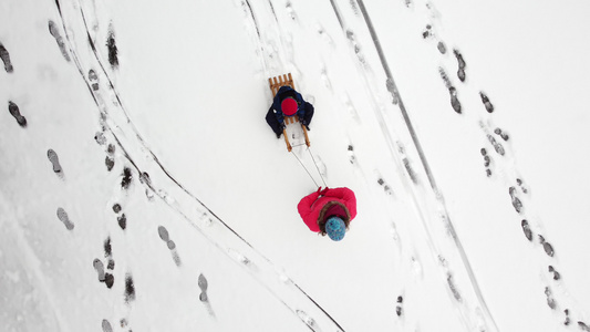 母亲在新鲜的雪地上用雪橇拉着孩子从上面可见的脚印女人视频
