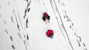 母亲在新鲜的雪地上用雪橇拉着孩子从上面可见的脚印女人8秒视频