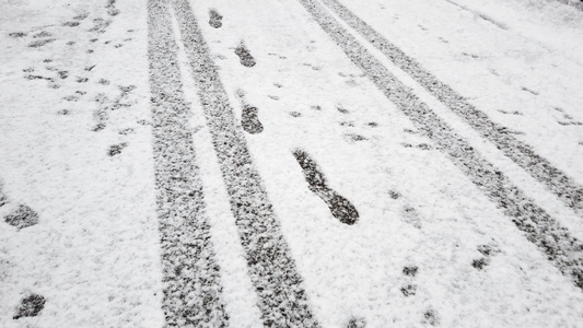 道路上新雪上的新雪上的脚印和轮胎足迹落下雪花视频